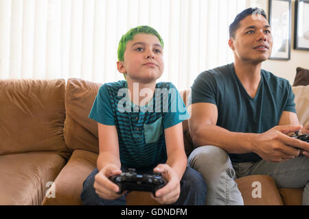 Vater und Sohn spielen Videospiel auf sofa Stockfoto