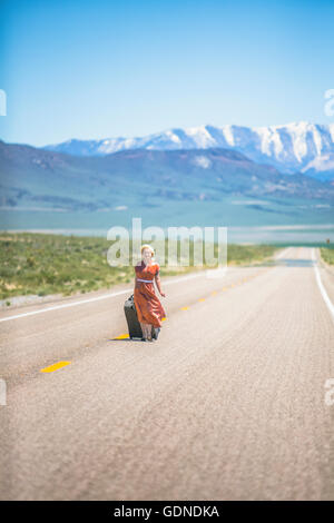 1950er Jahre junge Stil Frau allein zu Fuß auf der Autobahn 50 ziehen Rädern Koffer, Nevada, USA Stockfoto