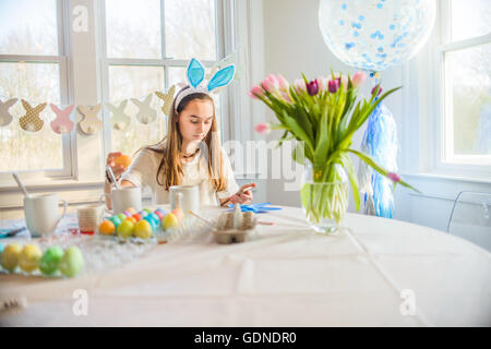 Teenager-Mädchen Texte zu lesen, während harte färben gekochten Eiern zu Ostern am Tisch Stockfoto