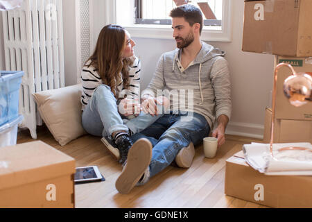 Umzug: junges Paar sitzt im Raum voller Kisten, trinken Heißgetränk Stockfoto