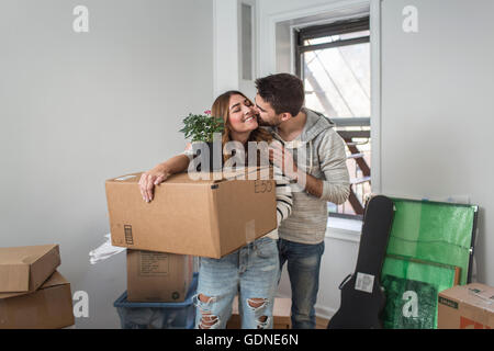 Umzug: junge Frau mit Karton, junger Mann auf Wange küssen Stockfoto
