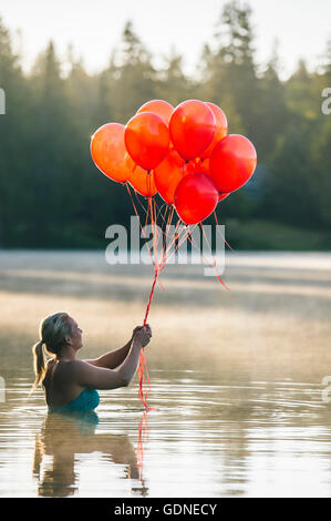 Frau im Wasser halten Haufen rote Luftballons Stockfoto