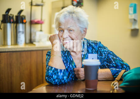 Graue dunkelhaarige Frau am Tisch, Blick auf die Kamera zu Lächeln Stockfoto