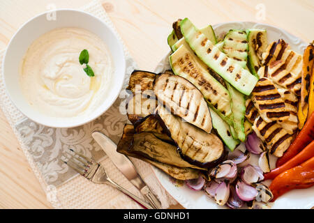 Draufsicht auf eine Platte mit gebratenem Gemüse und eine Schale mit Tahini-Sauce, eine gesunde Ernährung-starter Stockfoto