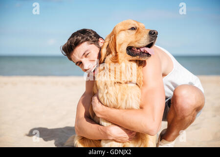 Fröhlichen jungen Mann lächelnd und umarmt seinen Hund am Strand Stockfoto