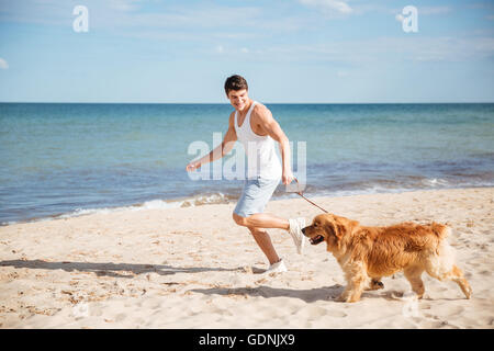Hübscher junger Mann lächelnd und läuft mit seinem Hund am Strand Stockfoto