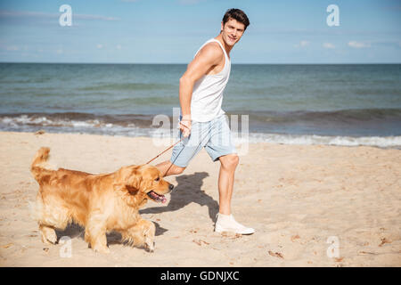 Attraktive junge Mann Joggen und Spaß mit seinem Hund am Strand Stockfoto