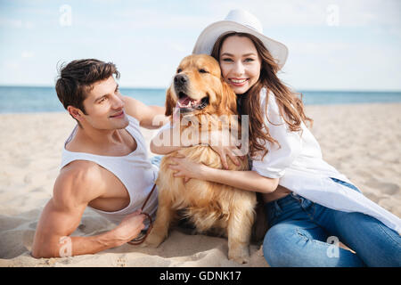 Junge glücklich lächelnde paar verliebt am Strand mit Hund sitzen Stockfoto