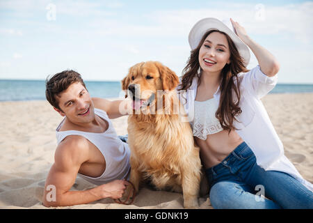 Junge glücklich lächelnde paar verliebt am Strand mit Hund sitzen Stockfoto
