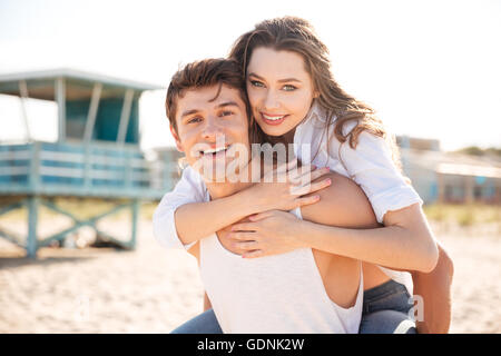 Porträt von fröhlichen jungen Mann seiner Freundin am Strand Huckepack Stockfoto