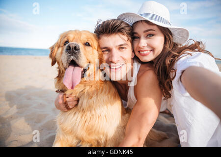 Porträt des jungen Brautpaares umarmt ihren Hund und lächelnd am Strand Stockfoto