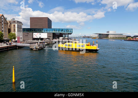 Ein gelbe Hafen Bus kommt an das Königliche Schauspielhaus im Hafen von Kopenhagen. Das königliche Opernhaus gegenüber weiter entfernt. Stockfoto