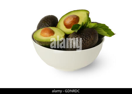 Frische gesunde ganze und halbierte Avocados in Zitronensaft in weiße Runde Schüssel mit Basilikumblättern auf sauberen, weißen Hintergrund bedeckt Stockfoto