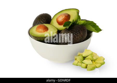 Frische gesunde ganze und halbierte Avocados in Zitronensaft in weiße Schüssel mit Basilikumblättern auf sauberen, weißen Hintergrund bedeckt Stockfoto