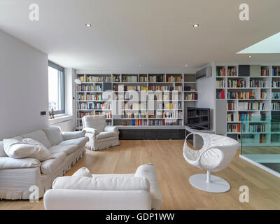 Innenansicht aus einem modernen Wohnzimmer mit großen Bücherregal und Holzboden im Vordergrund zwei weiße Sessel und ein sofa Stockfoto
