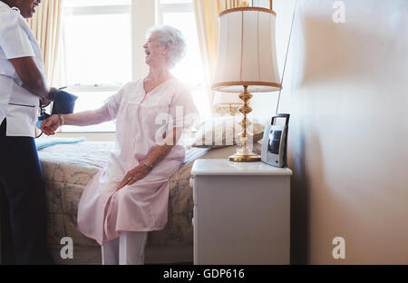 In Innenräumen geschossen Sie glücklich senior Frau auf Bett sitzend mit Krankenschwester Blutdruck überprüfen. Nach Hause Pflegeperson Tests Blut beding Stockfoto