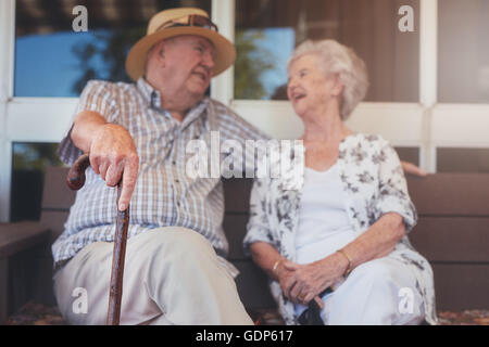 Porträt von senior Brautpaar sitzen auf einer Bank vor ihrem Haus. Älteres Ehepaar entspannen im Freien lieben. Stockfoto