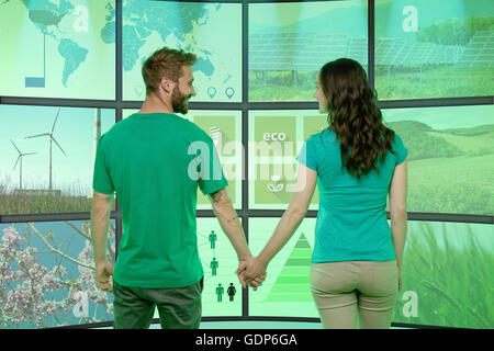 Junges Paar Hand in Hand, stehend vor grafischen Bildschirmen Umwelt Bilder anzeigen Stockfoto