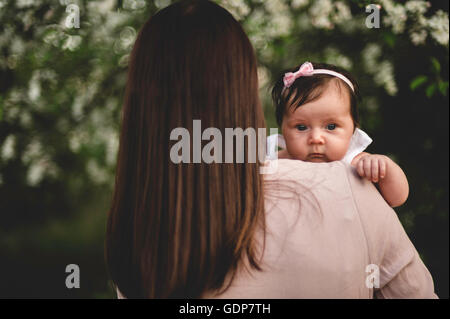 Über Schulter Porträt Babymädchen in armen Mütter im Garten Stockfoto