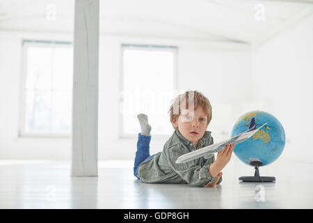 Porträt eines jungen auf Boden mit Globus und Spielzeug Flugzeug spielen Stockfoto