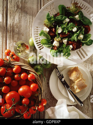 Mediterraner Salat, Feta-Käse, schwarze Oliven, Sonne getrocknete Tomaten, Salatblätter mit frischen Tomaten in Korb, Draufsicht Stockfoto
