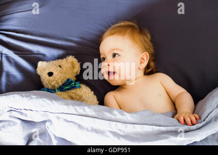 Babymädchen mit Teddybär im Bett liegend Stockfoto