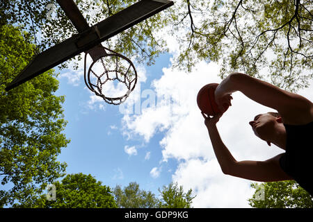 Niedrigen Winkel Blick auf Silhouette junger Mann, mit dem Ziel Kugel am Basketballkorb Stockfoto