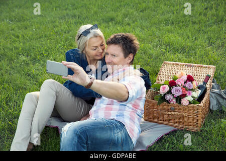 Älteres Paar auf Rasen mit Picknick, nehmen selfie Stockfoto