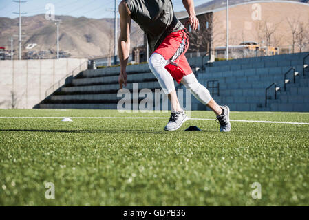 Hals abwärts Blick auf junge Mann läuft dabei Beweglichkeitstraining mit Markern auf Spielfeld Stockfoto