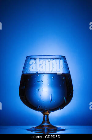 Wasserglas mit Flüssigkeit Tropfen und Spritzer auf einem blauen Hintergrund Licht Stockfoto