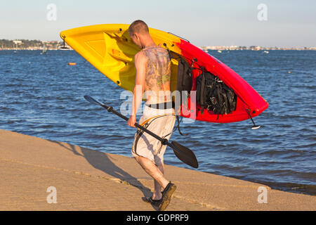 Mann mit Tattoos auf Rücken mit Kajak, nach Kajak rund um den Hafen von Poole im Juli Stockfoto