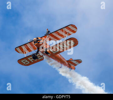 Orange Boeing Stearman Doppeldecker, die Bestandteil der Breitling Wingwalker Kunstflug Ausbildungs-Team in blauer Himmel mit weißen Rauch Stockfoto