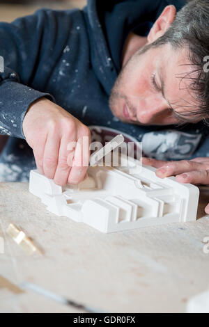 Ein Kaukasischen Männchen in Farbe bespritzt-Hoodie mit einem Präzisions-Messer und Bildhauerei eine weißen Gipsmodell auf dem Schreibtisch. Stockfoto