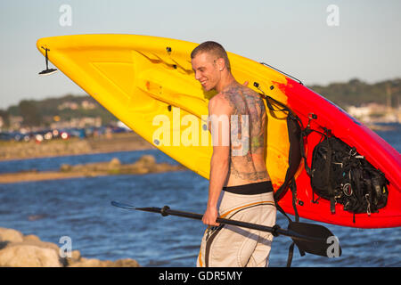 Mann mit Tattoos auf Rücken mit Kajak, nach Kajak rund um den Hafen von Poole im Juli Stockfoto