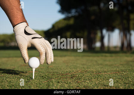 Nahaufnahme des Golf Spieler Hand Ball am Abschlag zu platzieren. Schöner Sonnenaufgang am Golfplatz Landschaft im Hintergrund Stockfoto