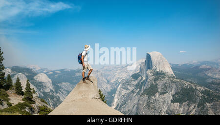 Junger Mann auf Felsvorsprung stehend, mit Blick auf den Half Dome, Blick vom Glacier Point, Yosemite-Nationalpark, Kalifornien, USA Stockfoto