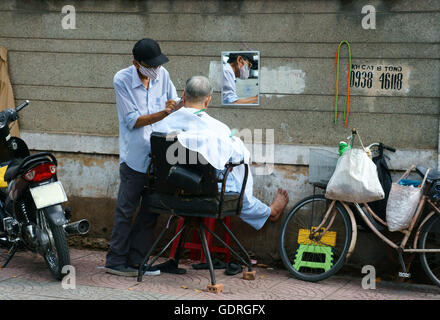 Traditionelle Lebensweise der armen Menschen in Asien urban, vietnamesische männliche Friseur Arbeit im Freiluft-Shop auf Bürgersteig Stockfoto