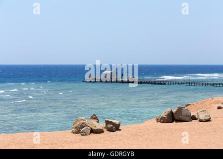 im Roten Meer in Ägypten Küste mit Sand und Steinen und Tauchen Pier im Hintergrund. Ruhige Szene mit blauem Wasser und Himmel Stockfoto