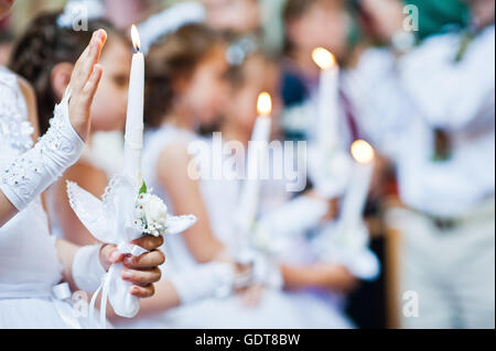 Hände mit Kerzen von kleinen Mädchen auf erste Heilige Kommunion Stockfoto