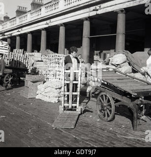 1950er-Jahren, historische Bild zeigt eine männliche Träger außerhalb des Covent Garten Obst und Gemüse Marktes mit seinem Wagen, London, England. Stockfoto