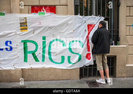 Banner an der Fassade einer Bank in Passeig de Gracia und Mann mit einer ATM-Proteste gegen die bedrückende soziale Situation. Spani Stockfoto