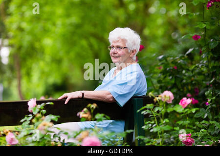 Glücklich senior Behinderte Dame mit einer Gehbehinderung, genießen Sie einen Spaziergang in einem sonnigen Park schieben ihre Gehhilfe oder Rollstuhl Stockfoto