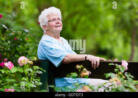 Glücklich senior Behinderte Dame mit einer Gehbehinderung, genießen Sie einen Spaziergang in einem sonnigen Park schieben ihre Gehhilfe oder Rollstuhl Stockfoto