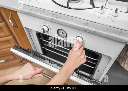 Weibliche Hand beinhaltet Backofen in der Küche. Close-up. Stockfoto
