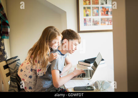 Schwester beobachten Bruder mit Laptop im Schlafzimmer Stockfoto