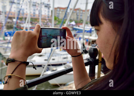 Frau, die ein Foto der Boote im Hafen mit Kamera-Handy Stockfoto