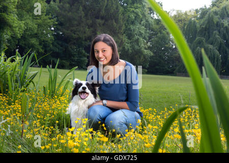 Junge Frau sitzt in einem Feld von Butterblumen mit ihrem Border-Collie Hund Stockfoto