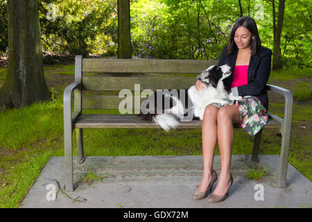 Junge Frau im Park sitzt auf einer Holzbank mit ihrem Border-Collie Hund Stockfoto