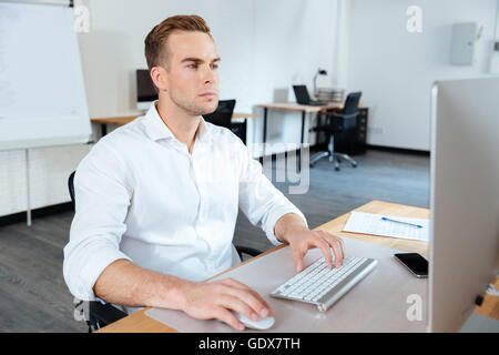 Attraktive fokussierte junger Geschäftsmann sitzt im Büro und computer Stockfoto