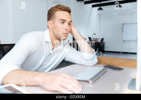 Traurig gelangweilter junger Geschäftsmann sitzen und arbeiten mit Computer im Büro Stockfoto